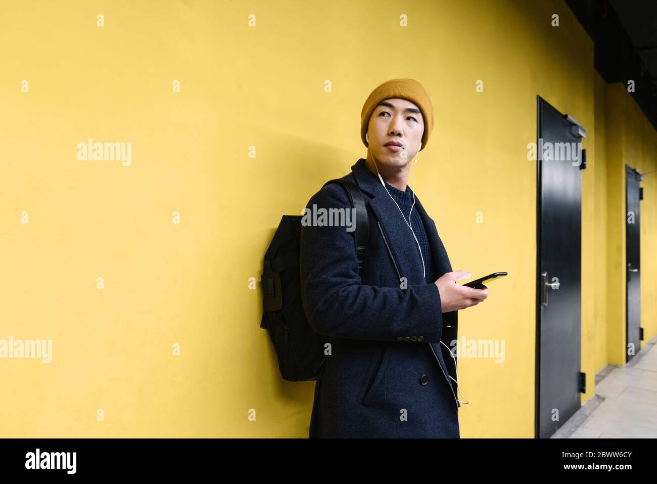Uomo elegante con cappello giallo e auricolari che utilizzano lo smartphone Foto Stock