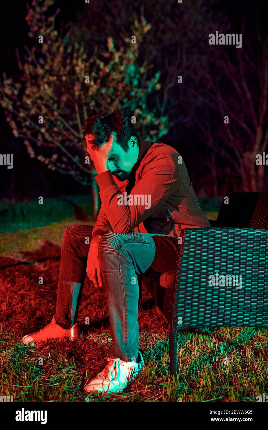Uomo triste seduto da solo sulla panchina del giardino di notte Foto Stock