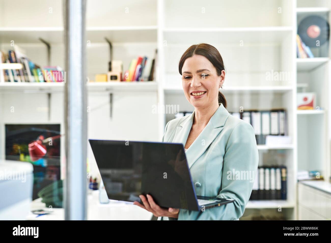 Donna d'affari sorridente in forma utilizzando il computer portatile in ufficio Foto Stock