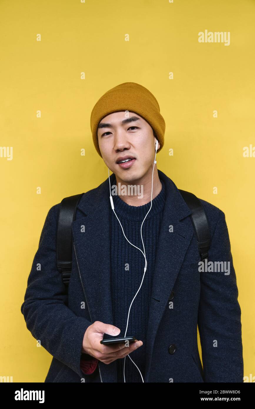 Ritratto di un uomo elegante con cappello giallo e auricolari utilizzando lo smartphone Foto Stock