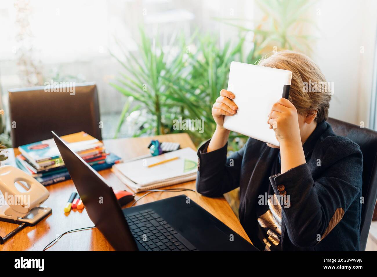 Ragazzo frustrato seduto alla scrivania con tablet e computer portatile Foto Stock