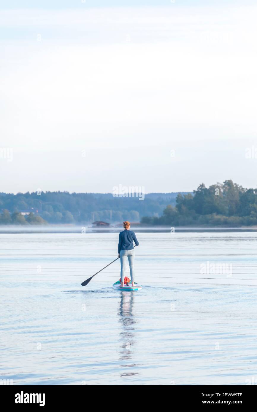 Donna in piedi su sup bordo al mattino su un lago Foto Stock