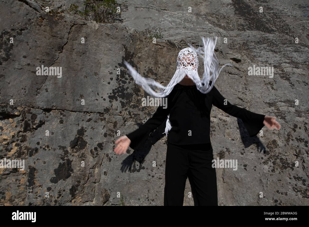 Donna che indossa un copricapo bianco con frange che si muovono davanti alla parete rocciosa Foto Stock