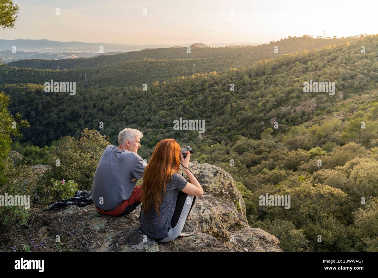 Padre e figlia adulta seduti sulla roccia godendo la vista al tramonto Foto Stock