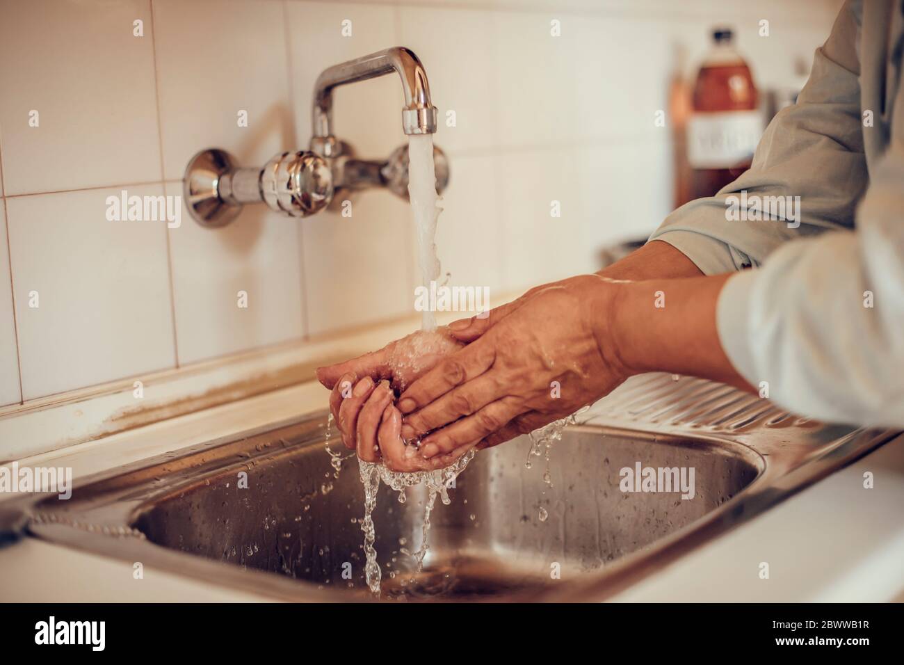 Primo piano di una donna che le lava le mani con sapone e acqua nel lavabo della cucina Foto Stock