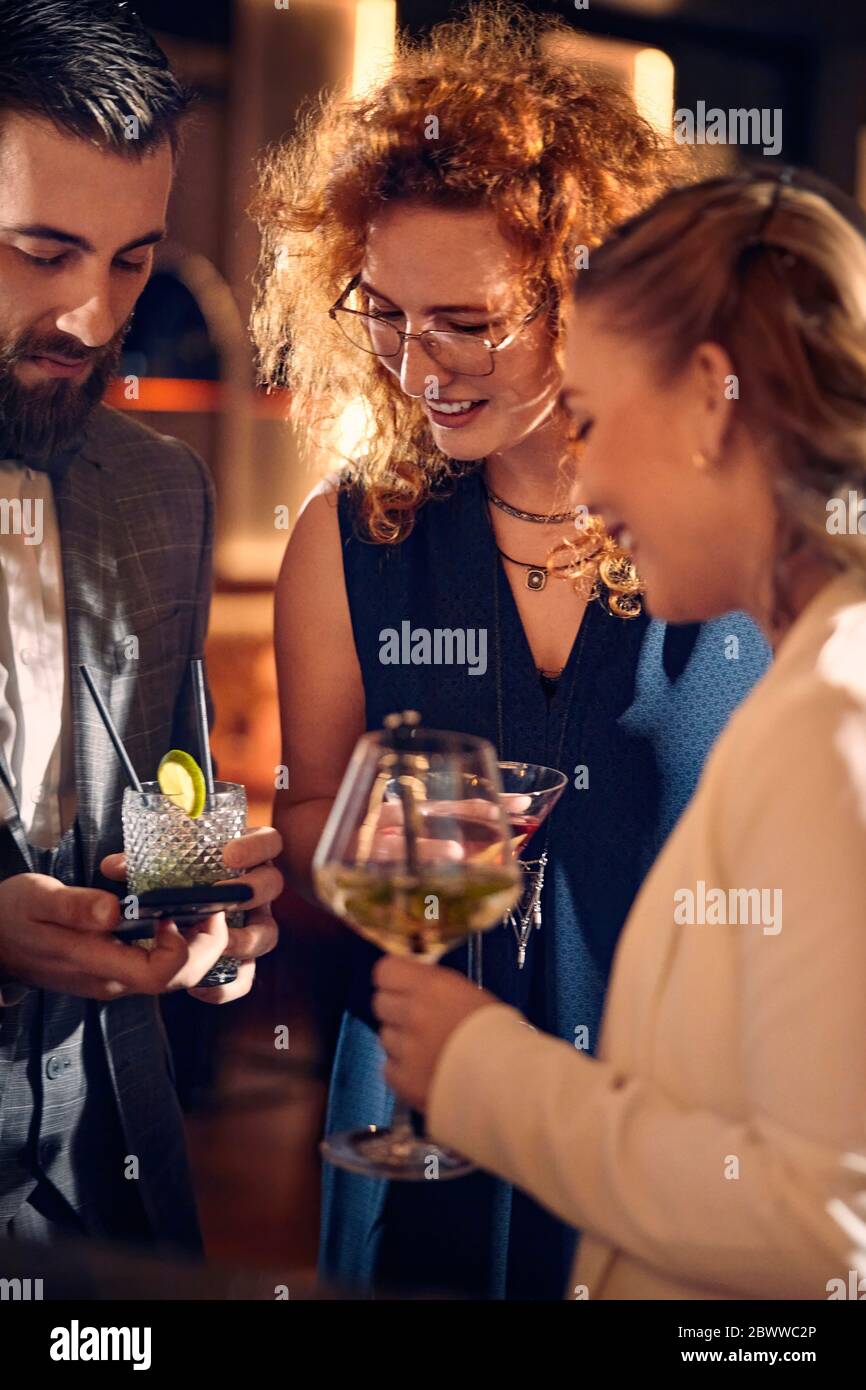 Amici con cocktail e smartphone socializzando in un bar Foto Stock