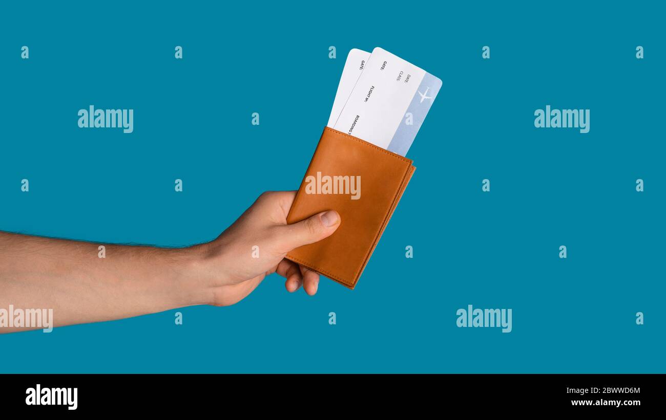 Restrizioni di viaggio dovute al coronavirus. Uomo con passaporto e biglietti aerei su sfondo blu, primo piano. Panorama Foto Stock