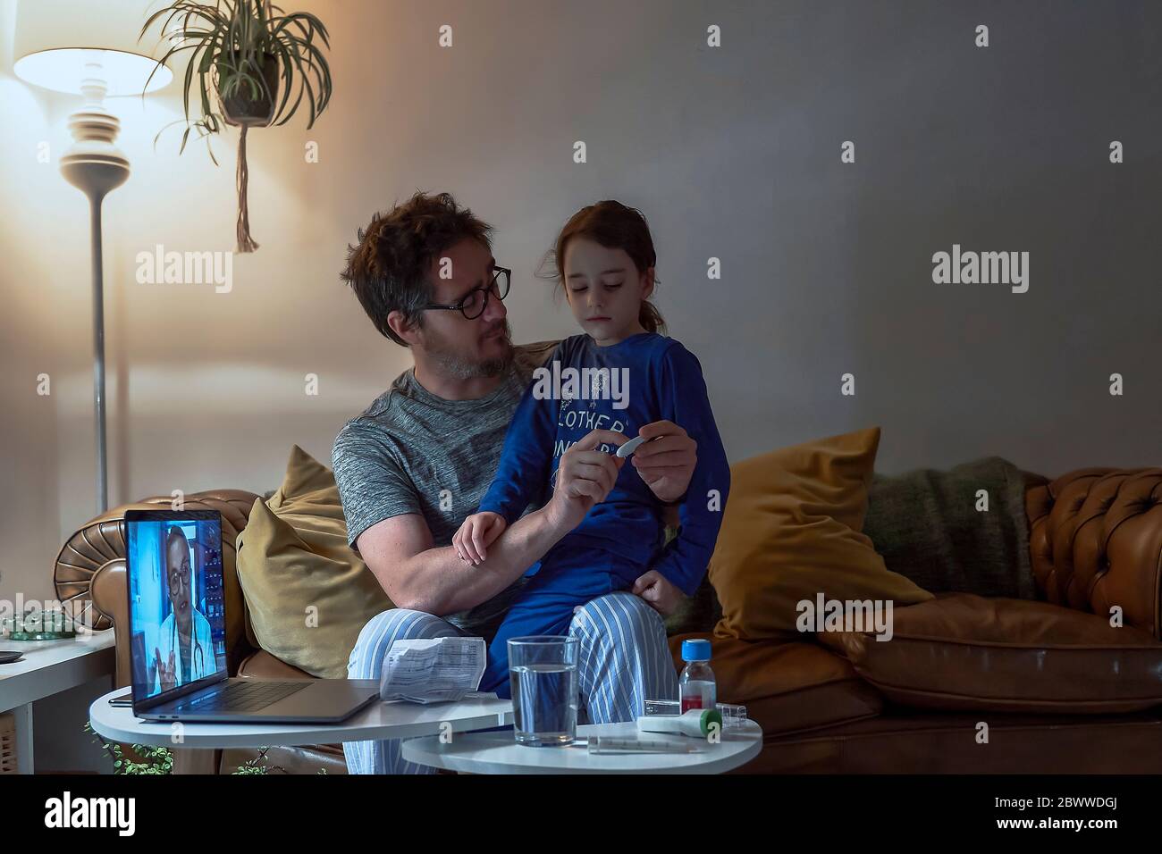 Uomo che tiene il termometro mentre si siede con la figlia malata durante la videochiamata a casa Foto Stock