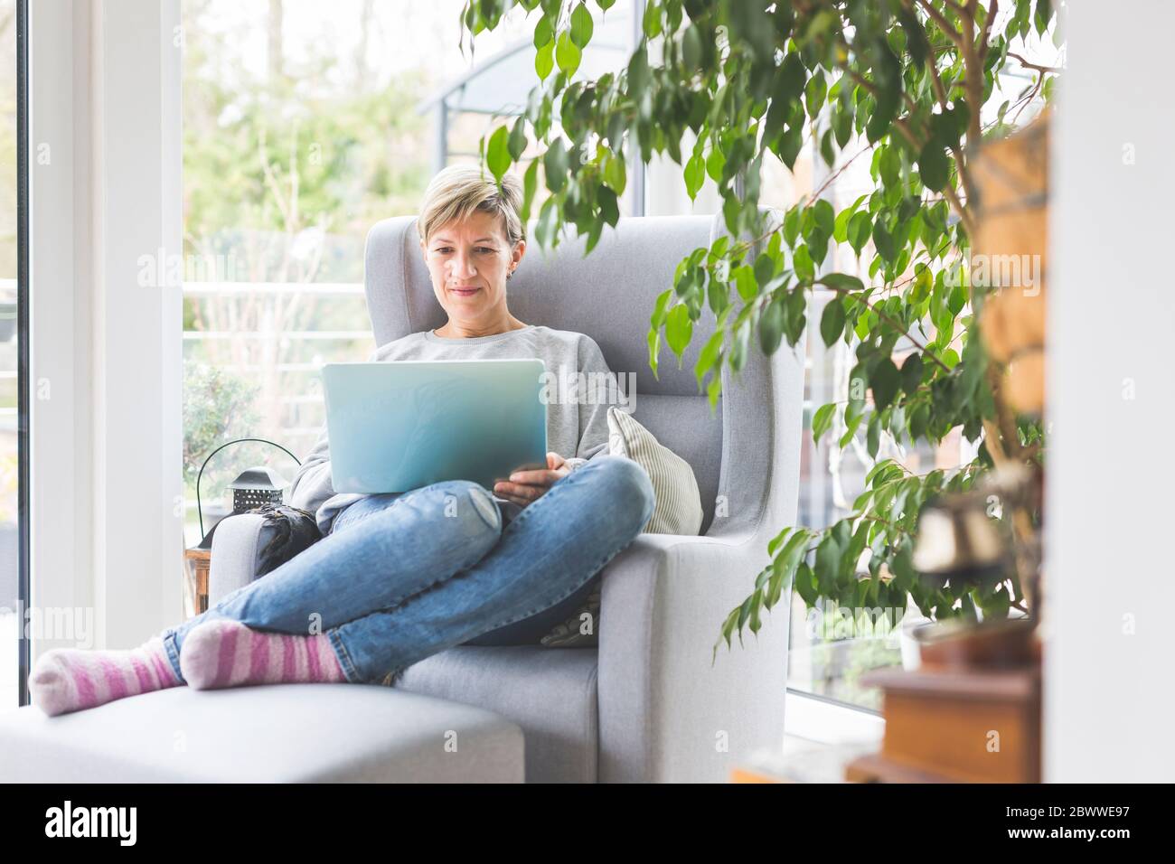 Donna matura che lavora da casa, con un computer portatile, seduta in poltrona Foto Stock