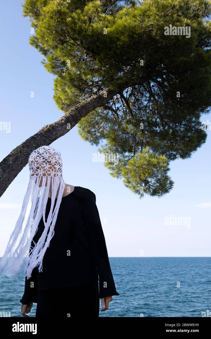 Donna che indossa un copricapo bianco con frange in piedi di fronte al mare Foto Stock