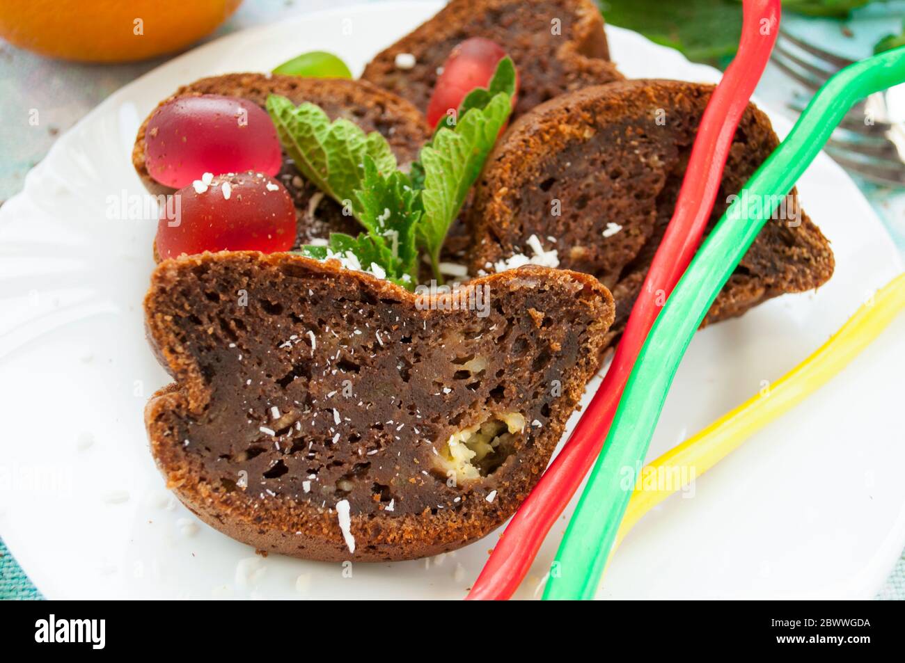 Pezzi di torta al cioccolato e caramelle di gelatina colorate cosparse di fiocchi di cocco su un piatto bianco decorato con primo piano di menta Foto Stock