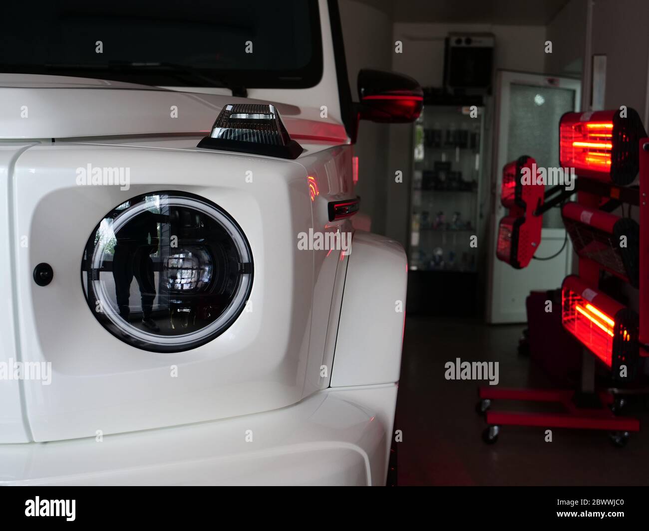 Di essiccazione a raggi infrarossi di parti di carrozzeria dopo applicazione di stucco e di vernice su un bianco off-road veicolo in officina di carrozzeria con lanterne rosse nella lavorazione Foto Stock