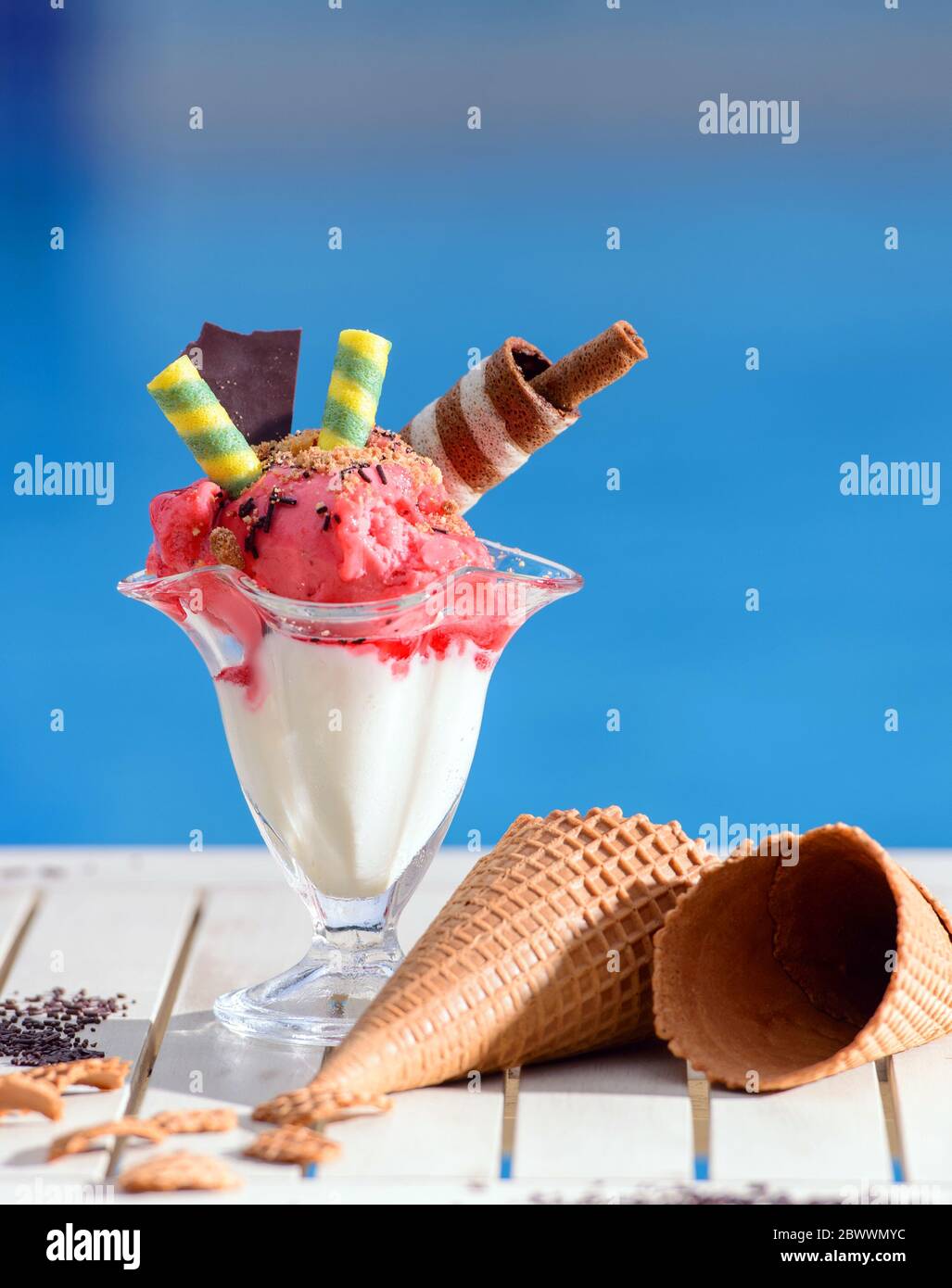 Primo piano di vetro con gelato alla fragola su sfondo bokeh sfocato con spazio di copia. Sorbetto al lampone con coni di cioccolato a base di waffle su un tavolo bianco o Foto Stock