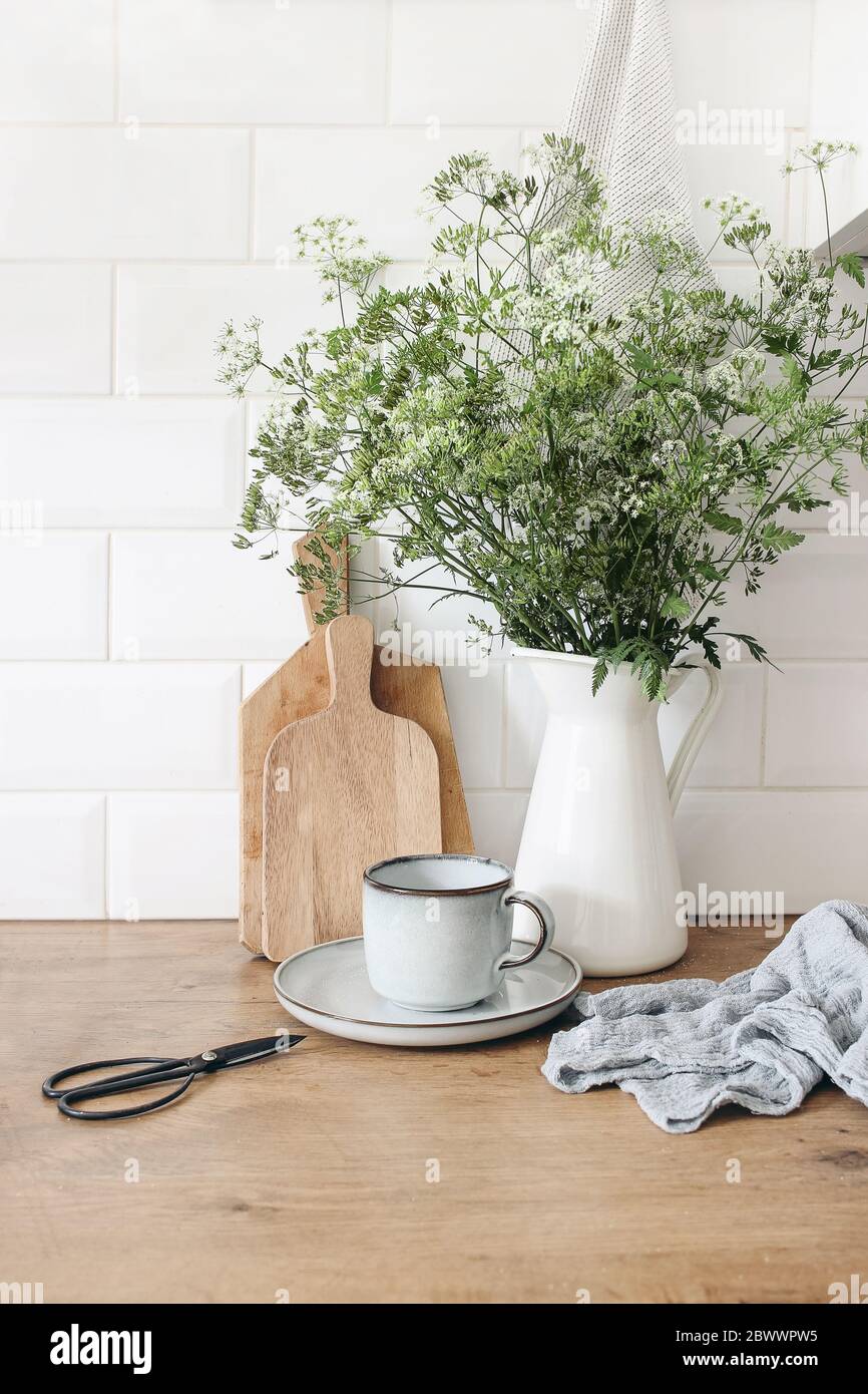 Cucina rustica interno. Composizione per la vita morta con tazza di caffè, tagliere in legno e bouquet di prezzemolo di mucca in caraffa. Muro di mattoni bianchi, metro Foto Stock