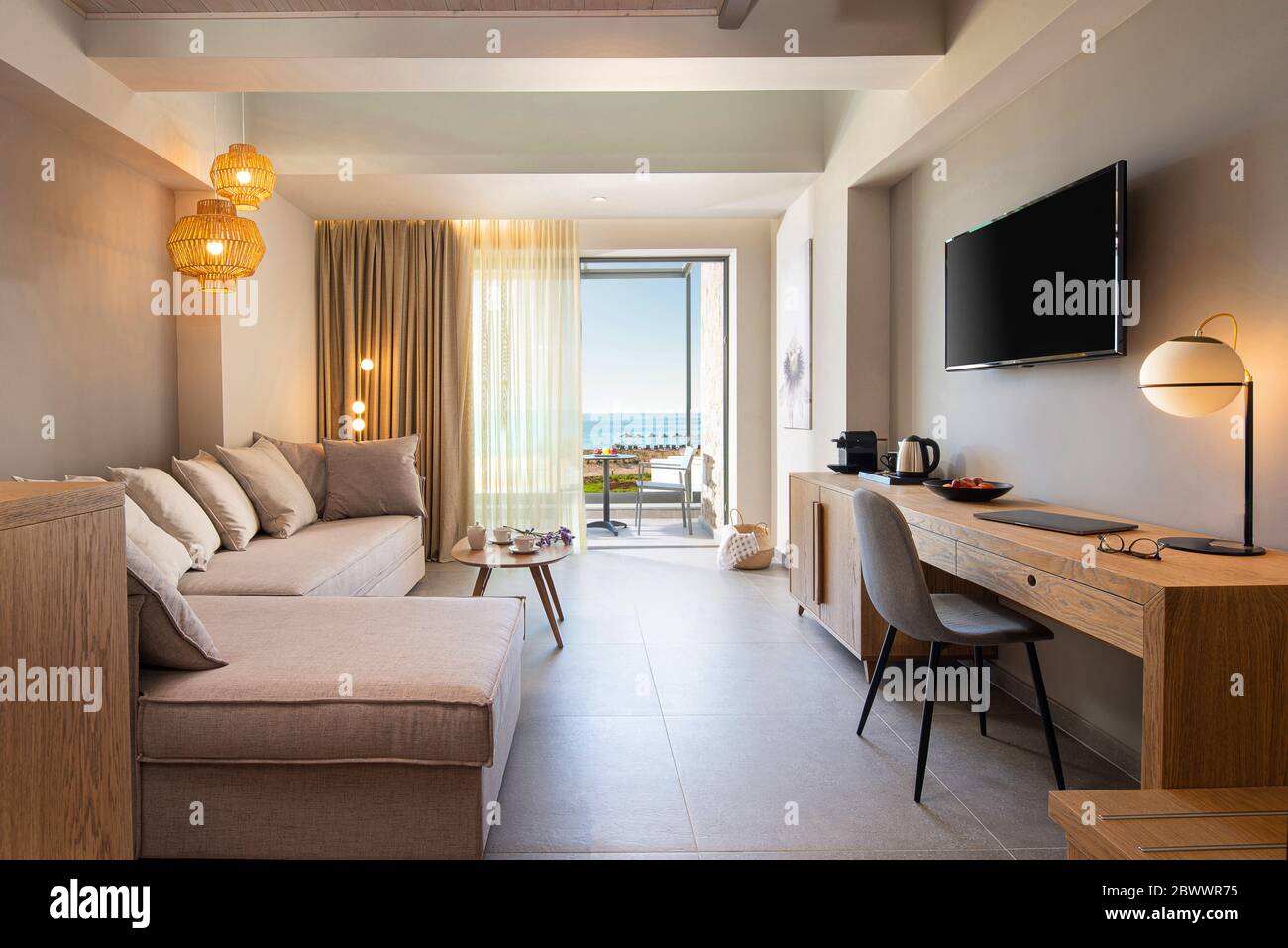 Interni in tessuto beige e legno di quercia chiaro con interni moderni del soggiorno con tavolo da lavoro e finestra a vista mare aperta Foto Stock