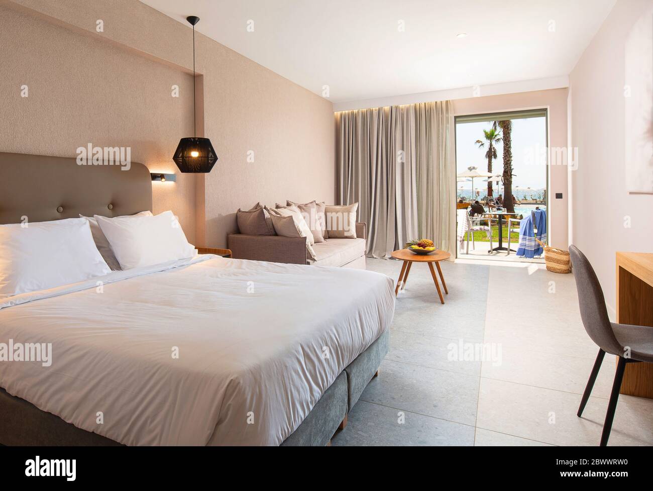 Interni dal design moderno della camera da letto dell'hotel con delicati arredi in tessuto e terrazza aperta con piscina tropicale Foto Stock
