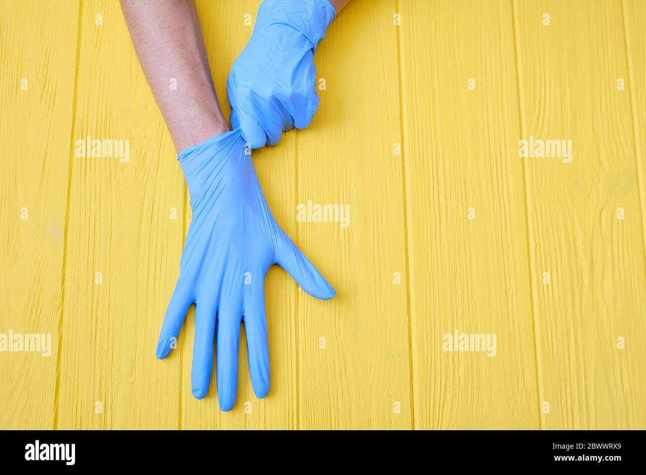 Guanti in nitrile blu. Mani di un medico nei guanti blu in lattice su uno sfondo giallo di legno con posto per il tuo testo Foto Stock