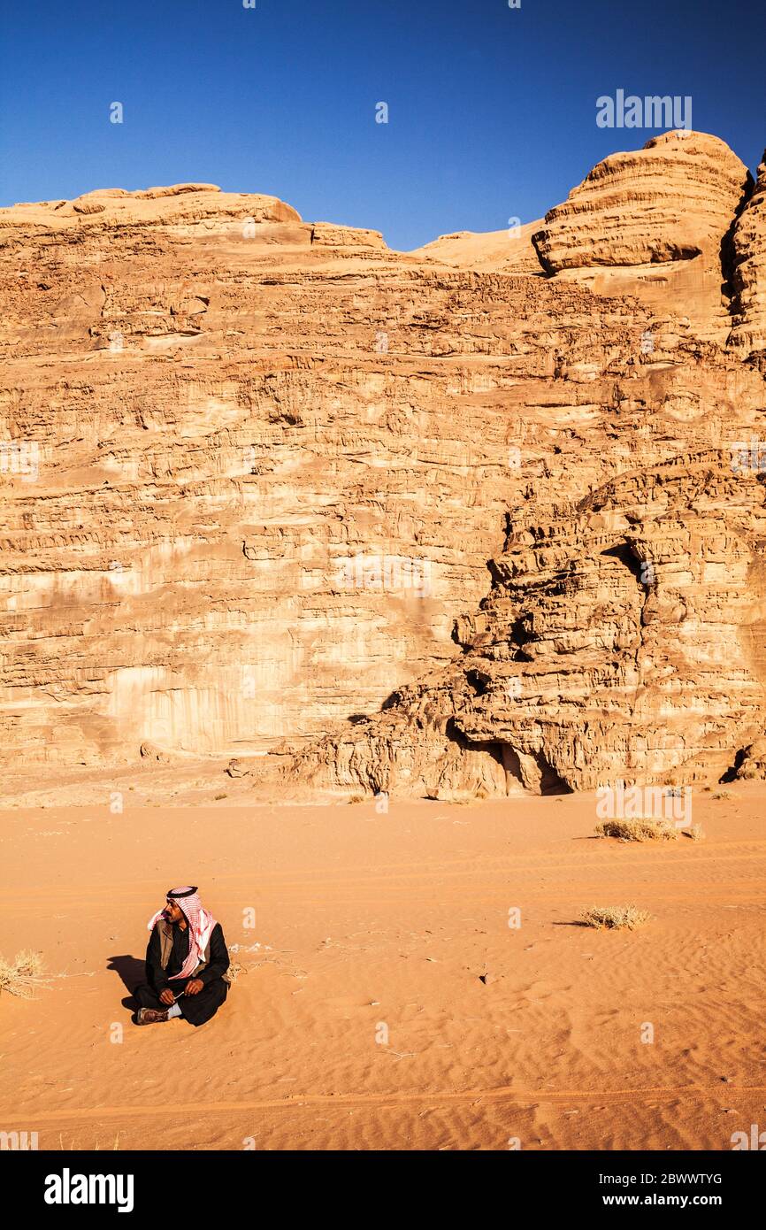 Un beduino uomo si siede sullo sfondo del deserto giordano a Wadi Rum o a valle della luna Foto Stock