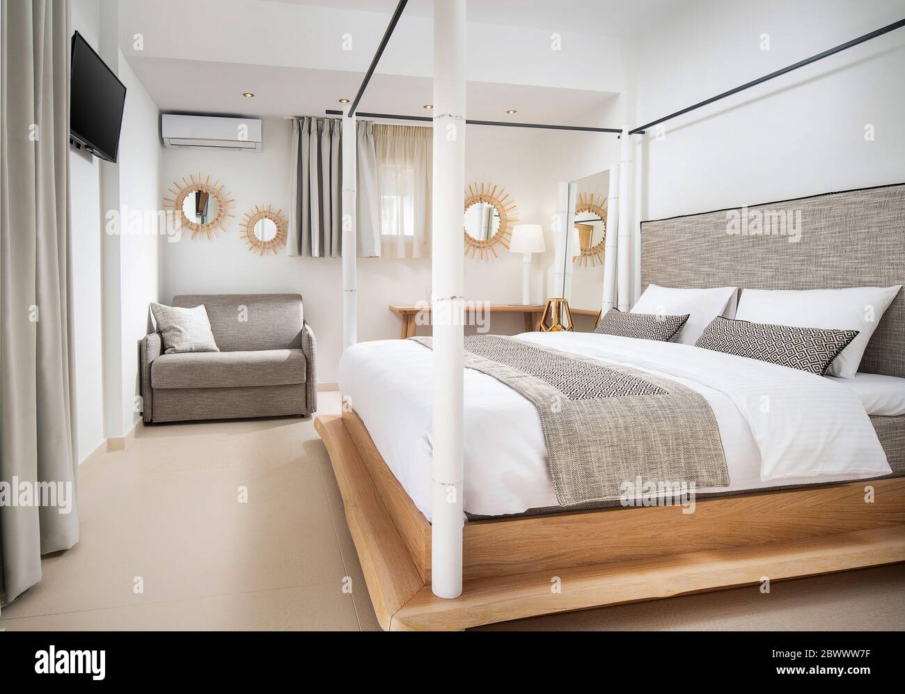 Interni chiari e vuoti di una moderna camera da letto in stile ecologico con mobili in legno, tessuti di cotone grigio, pareti bianche, pavimento in piastrelle di ceramica beige Foto Stock