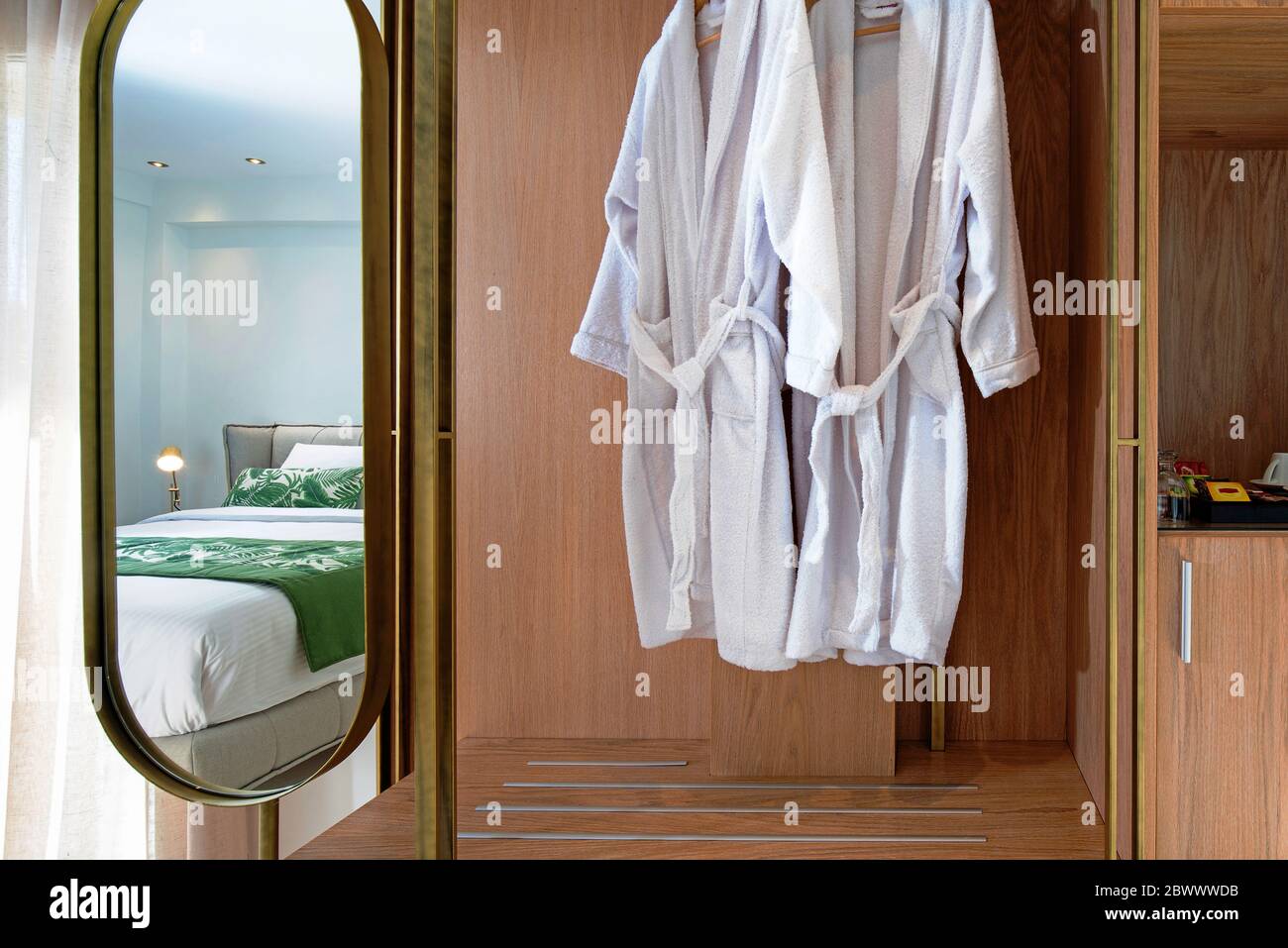 Vista frontale dell'armadio in legno con specchio e accappatoio bianco appeso nel moderno interno delle camere dell'hotel Foto Stock