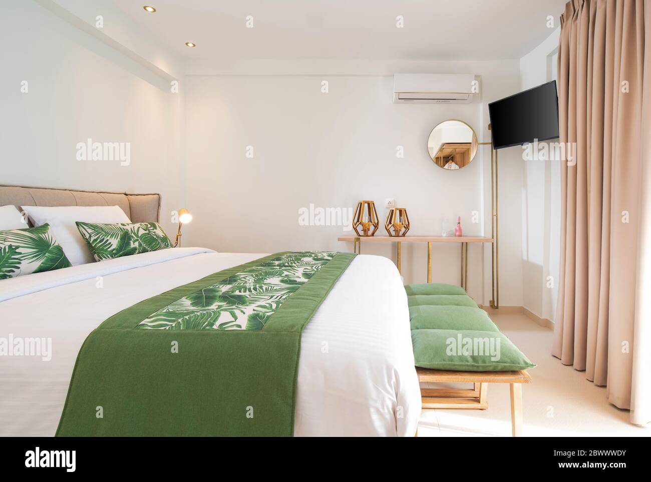 Interni moderni in stile ecologico delle camere dell'hotel con spazio vuoto per le copie delle pareti. Vista laterale della camera da letto bianca con lenzuola di foglie di palma verdi Foto Stock