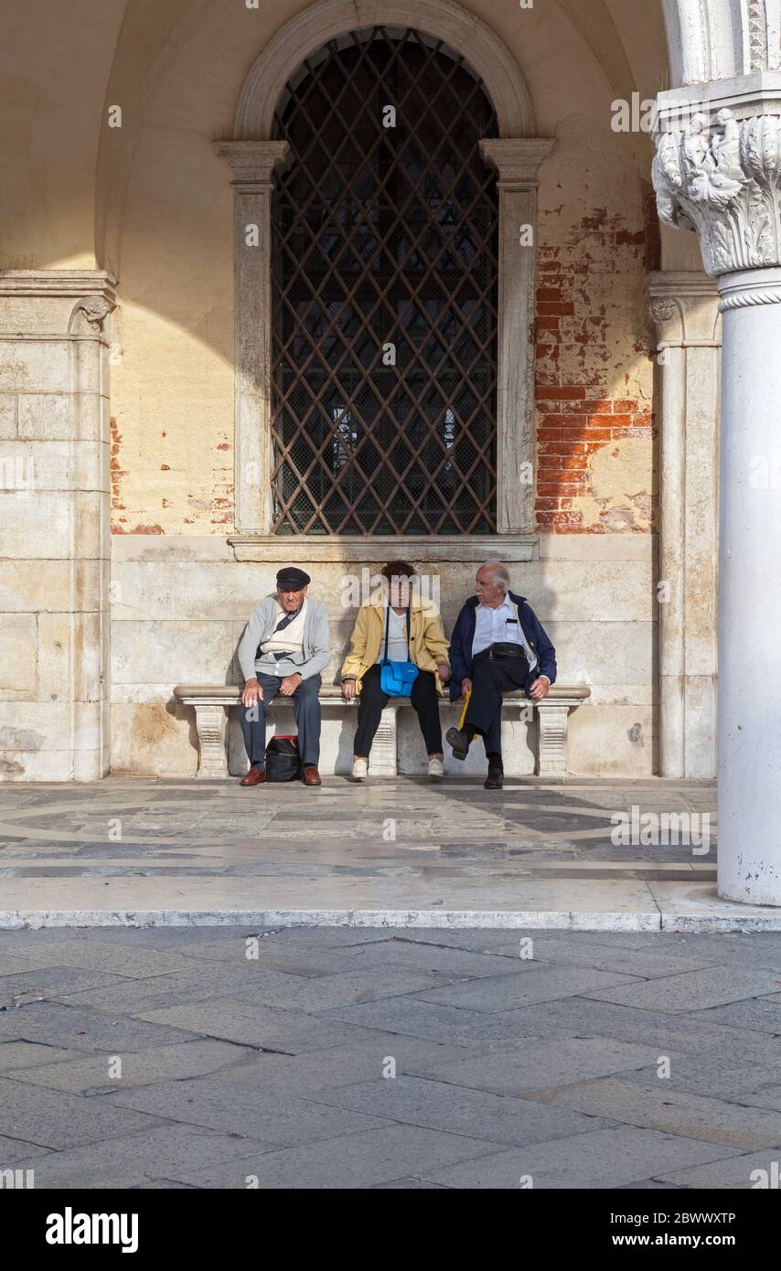 Tre turisti stanchi si rilassano su una panchina sotto e arco al Palazzo Ducale di Venezia Foto Stock