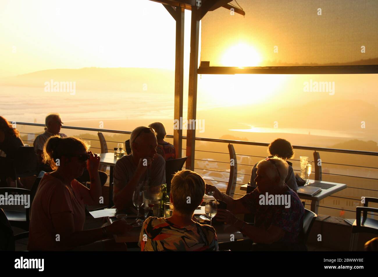 Wilderness, Sudafrica, Africa - Febbraio 2020: Terrazza di un ristorante sulla spiaggia e sagome degli ospiti in bella luce tramonto. Foto Stock