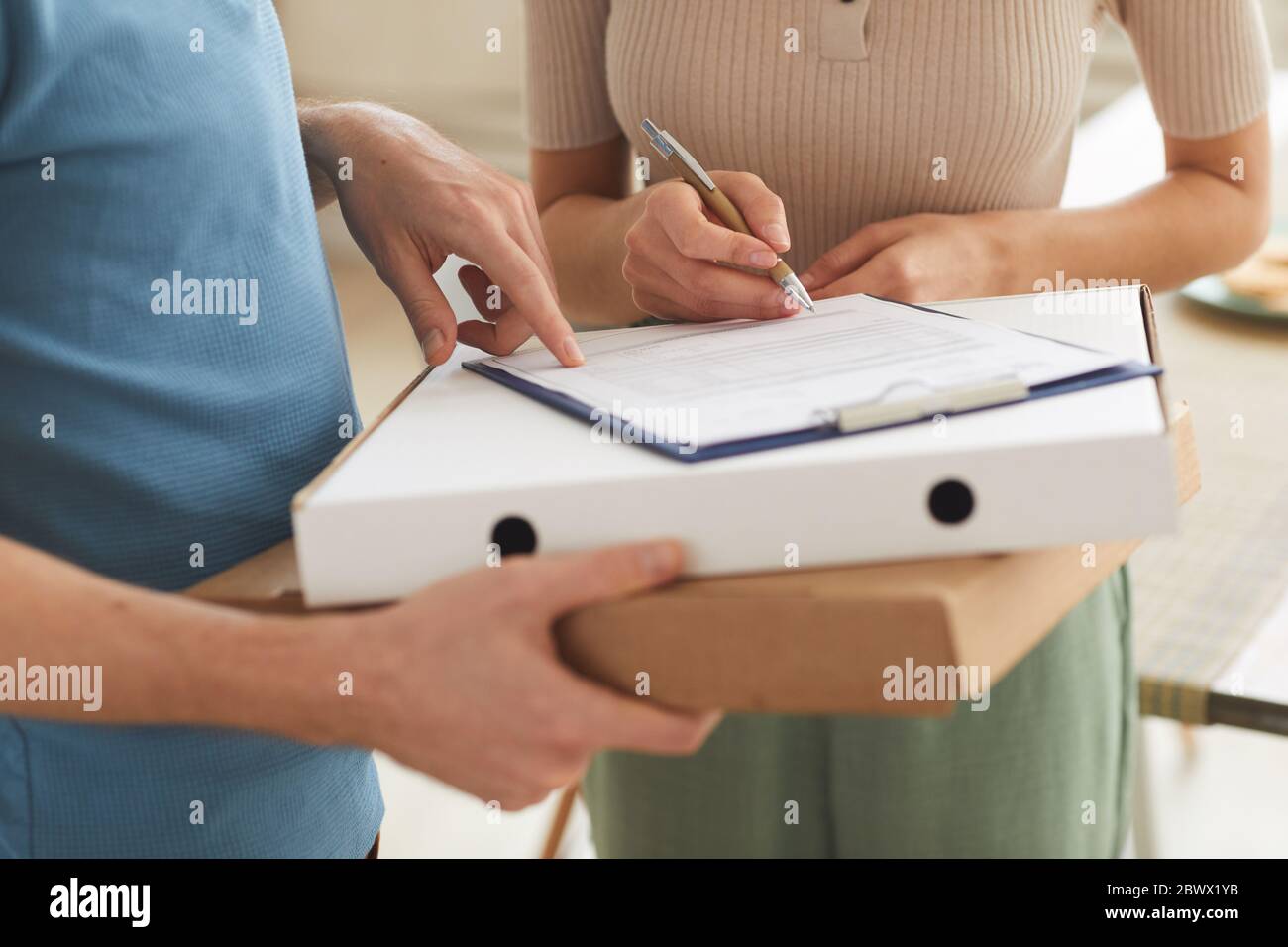 Primo piano di una donna che firma per la consegna e che prende la pizza dall'uomo di consegna Foto Stock