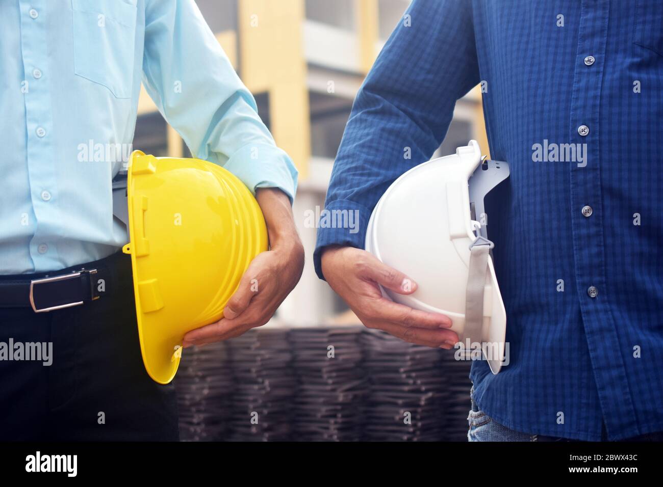 Due ingegneri che tengono in mano il cappello di sicurezza in piedi in costruzione sfondo Foto Stock