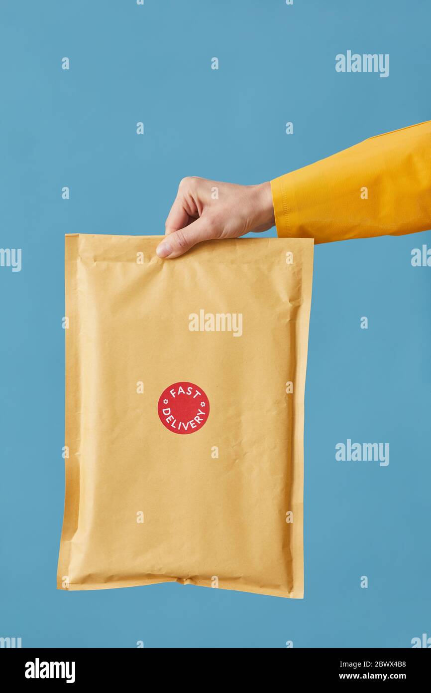 Primo piano del pacco di tenuta del postino imballato in carta isolata su sfondo blu Foto Stock