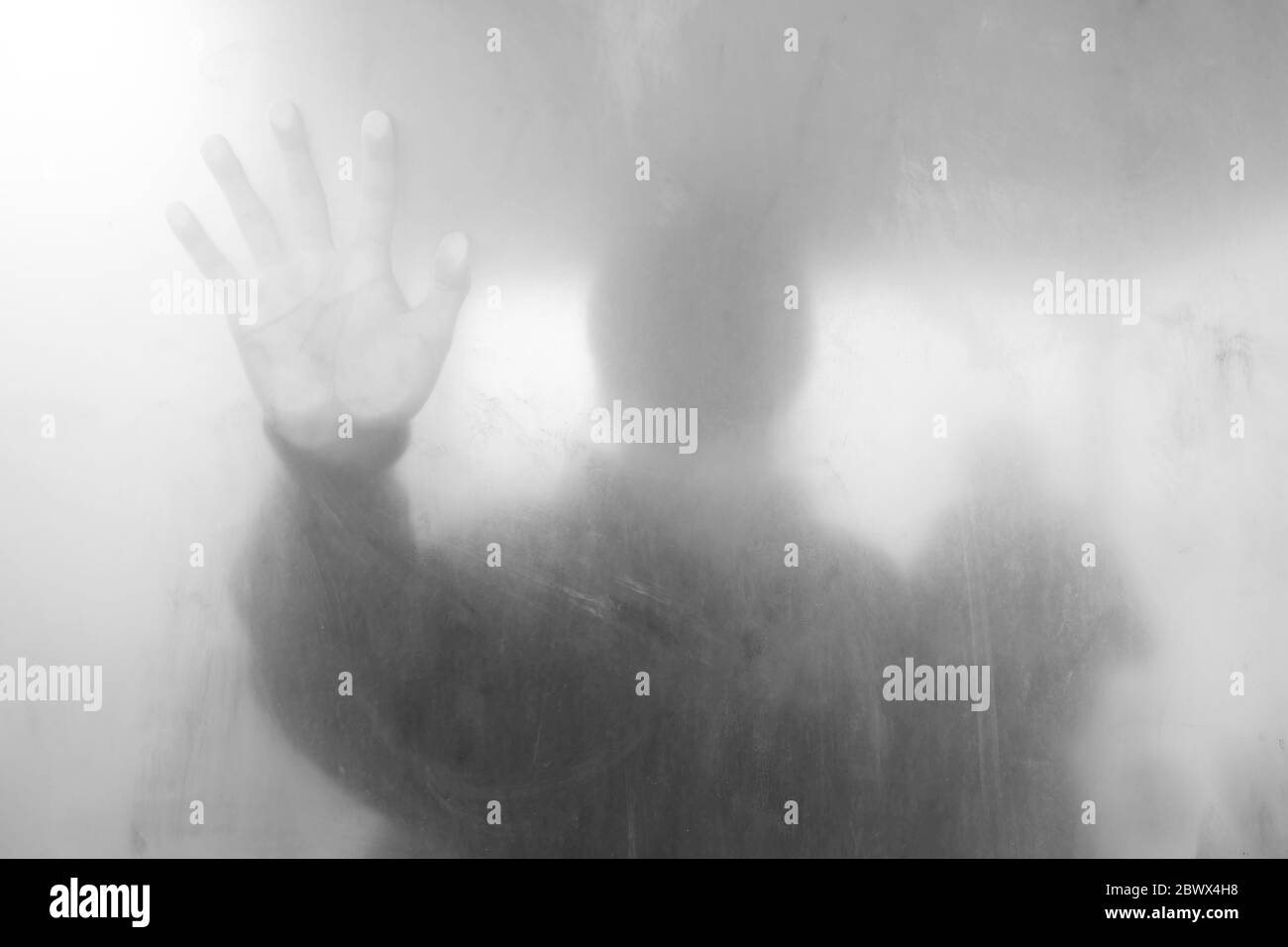 Giovane uomo in piedi dietro la parete bianca di vetro sporco, adatto per il concetto anonimo. Foto Stock