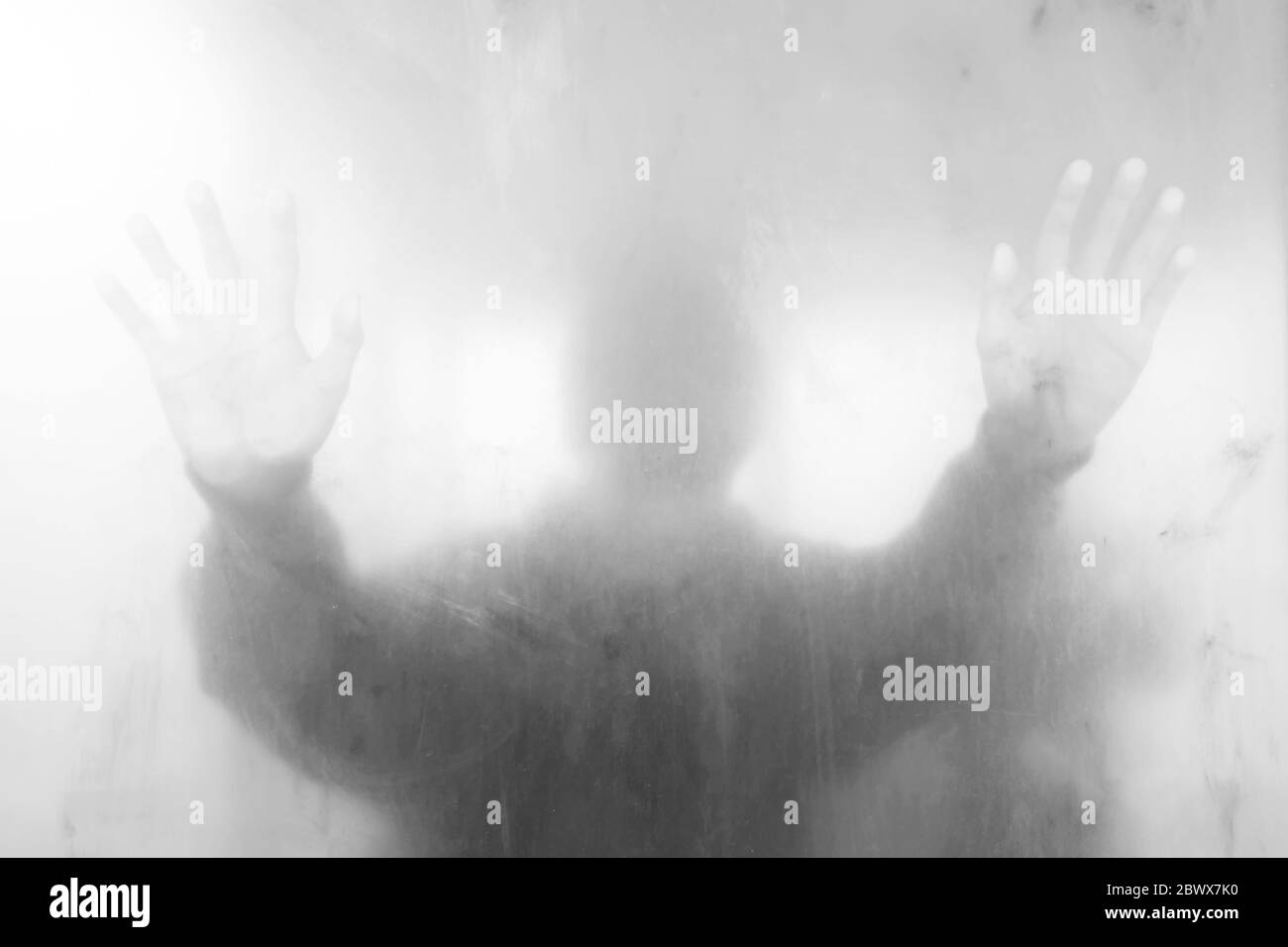 Giovane uomo in piedi dietro la parete bianca di vetro sporco, adatto per il concetto anonimo. Foto Stock