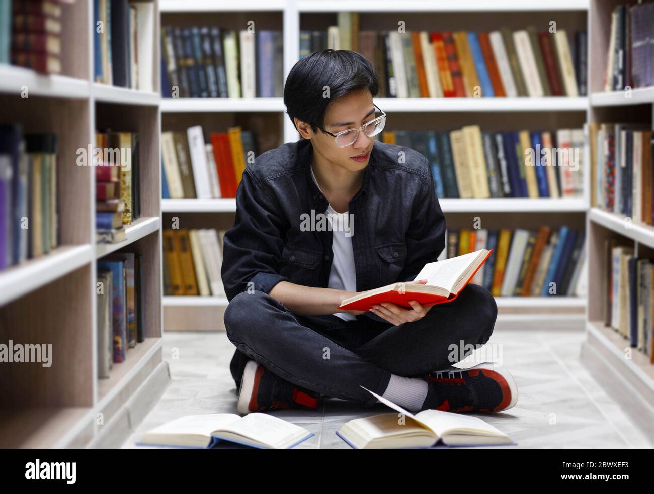 Ragazzo cinese messo a fuoco che legge libri alla biblioteca Foto Stock