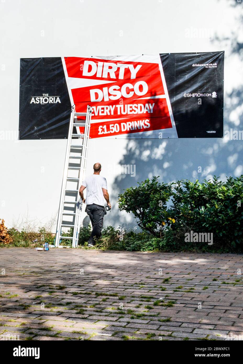 Un uomo con una scala che mette su un banner che fa pubblicità al 'Dirty disco) al Club Astoria a Portsmouth, Regno Unito Foto Stock