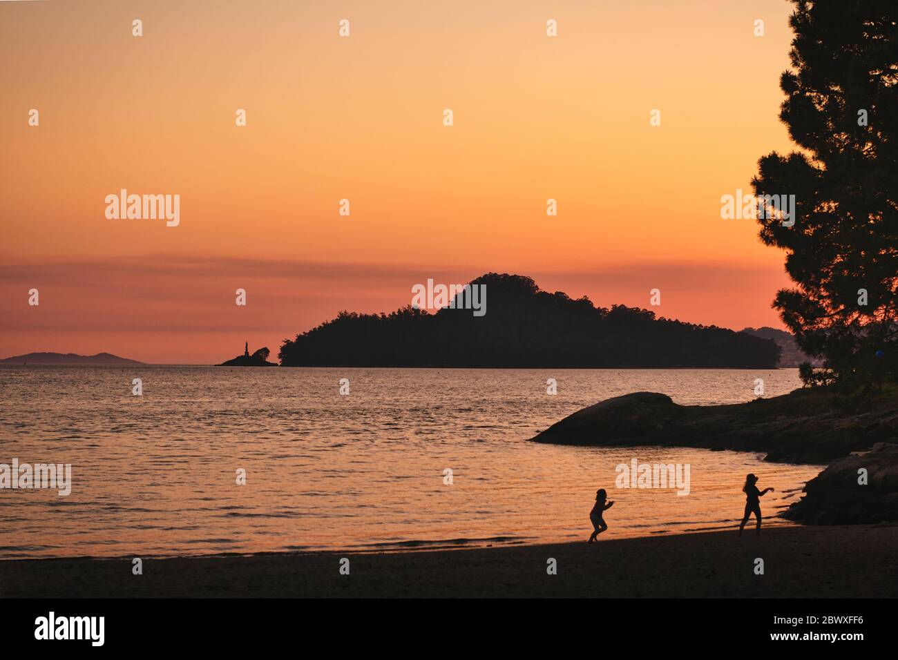 Vista dell'isola di Tambo dalla spiaggia di Lourido durante il tramonto con due silhoutes che giocano. Pontevedra, Galizia, Spagna. Foto Stock