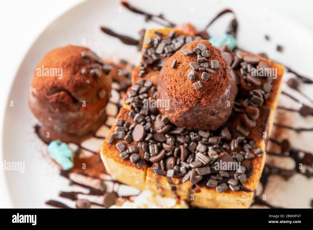 Primo piano vista dall'alto pane al Miele e paletta per gelato al cioccolato con sciroppo decorare con una pastiglia di cioccolato in un piatto bianco sul tavolo Foto Stock