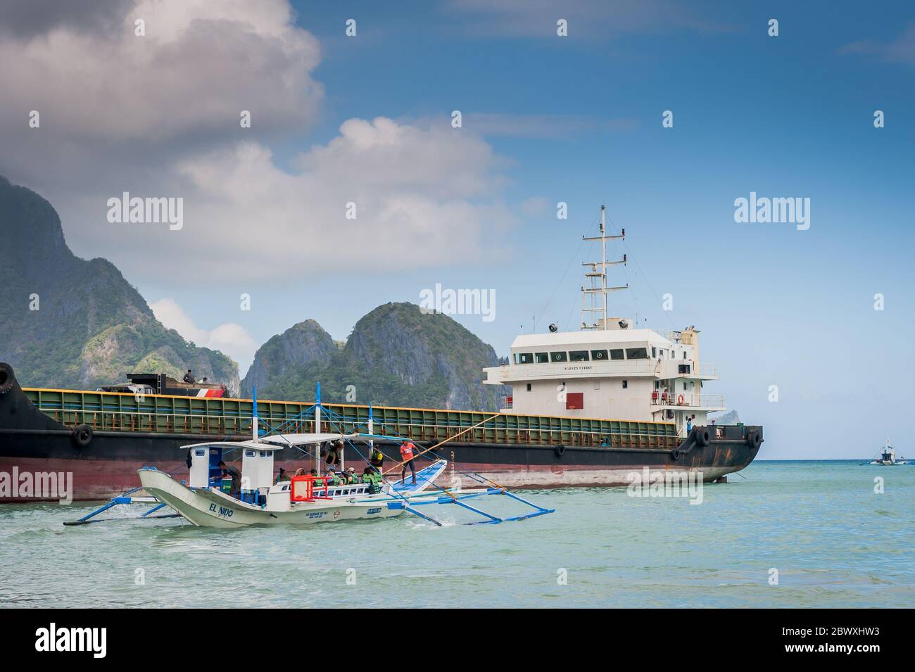 Una barca di pescatori dalla coda lunga carica di rifornimenti e turisti per fare una gita di un giorno con una enorme petroliera alle spalle dell'isola di El Nido, Filippine. Foto Stock