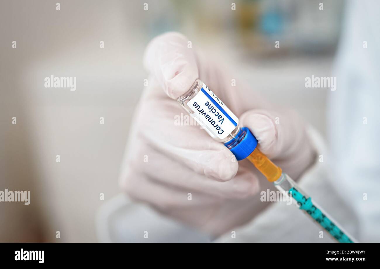 Mano in guanti medici bianchi che tengono siringa e vaccino del coronavirus (disegno proprio adesivo, dati fittizi), circa per iniettarlo closeup profondità poco profonda di fie Foto Stock