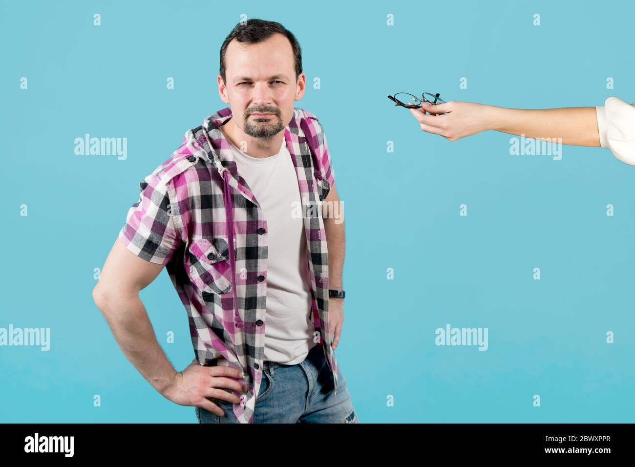 la mano femminile tiene fuori gli occhiali ad un tipo che vede male e squints per vedere qualcosa Foto Stock