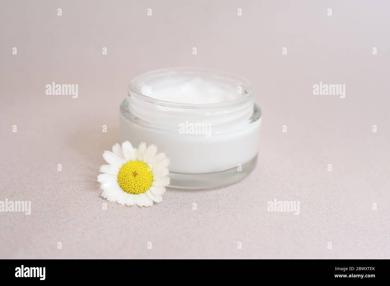 Vaso aperto di crema viso o corpo con un fiore camomilla vicino su sfondo beige. Concetto di cosmetica naturale. Prodotto naturale di bellezza con sp Foto Stock