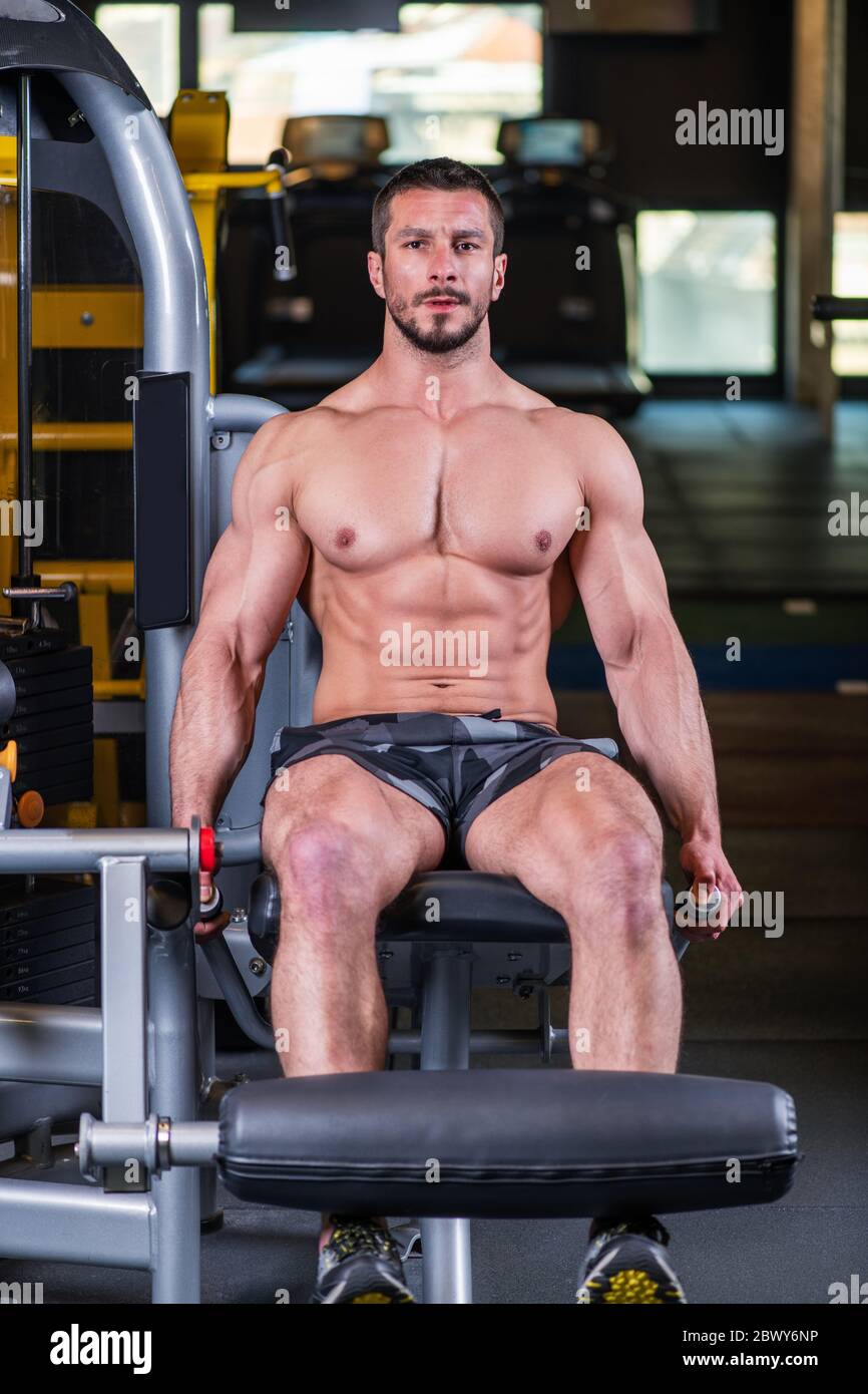 Uomo muscoloso sexy che fa esercizio di estensione delle gambe sulla macchina Foto Stock