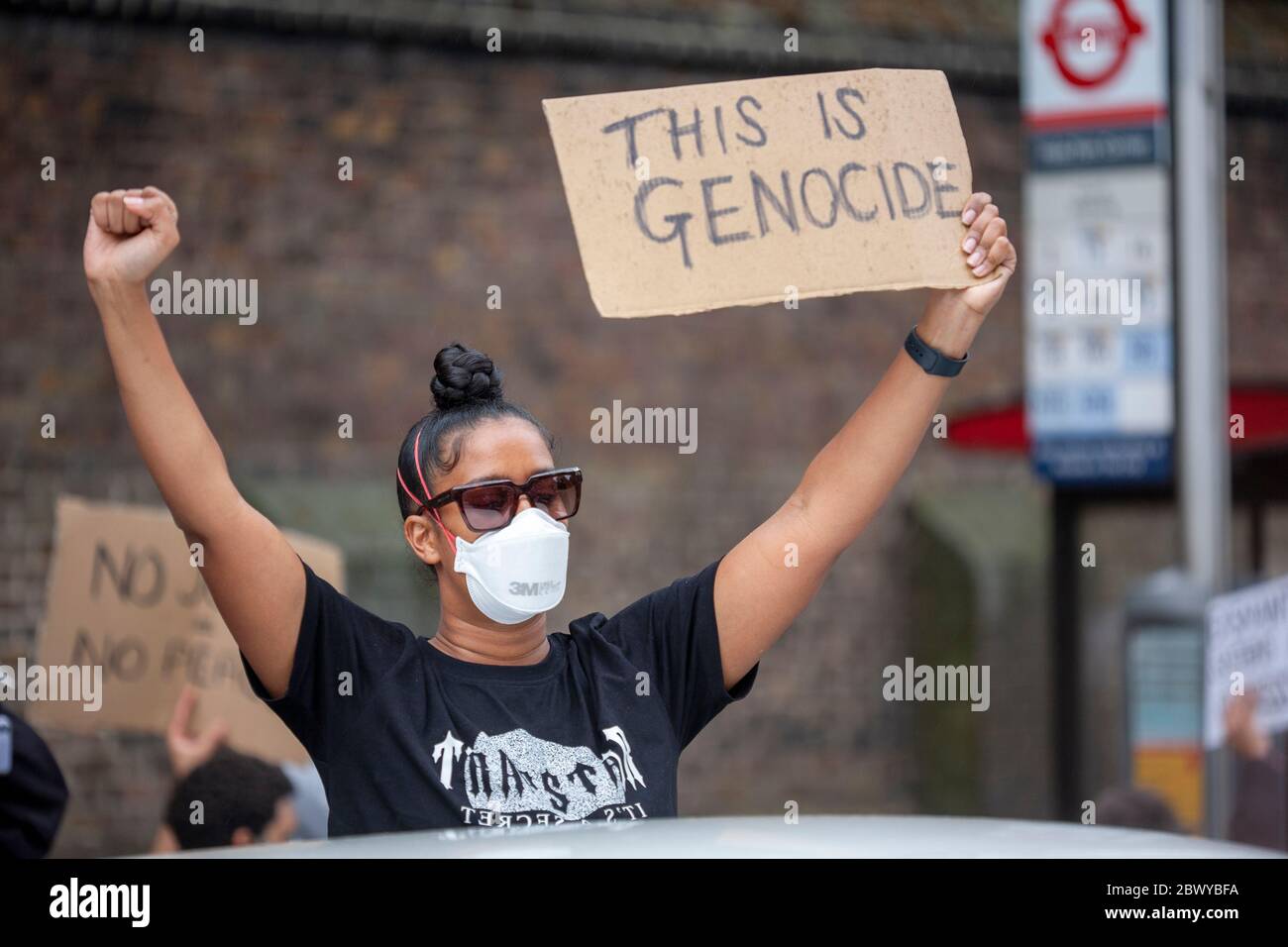 Donna che indossa una maschera chirurgica che tiene un segno 'questo è genocidio' fatto in casa durante la marcia Black Lives Matter protesta. Londra, Regno Unito, Inghilterra Foto Stock