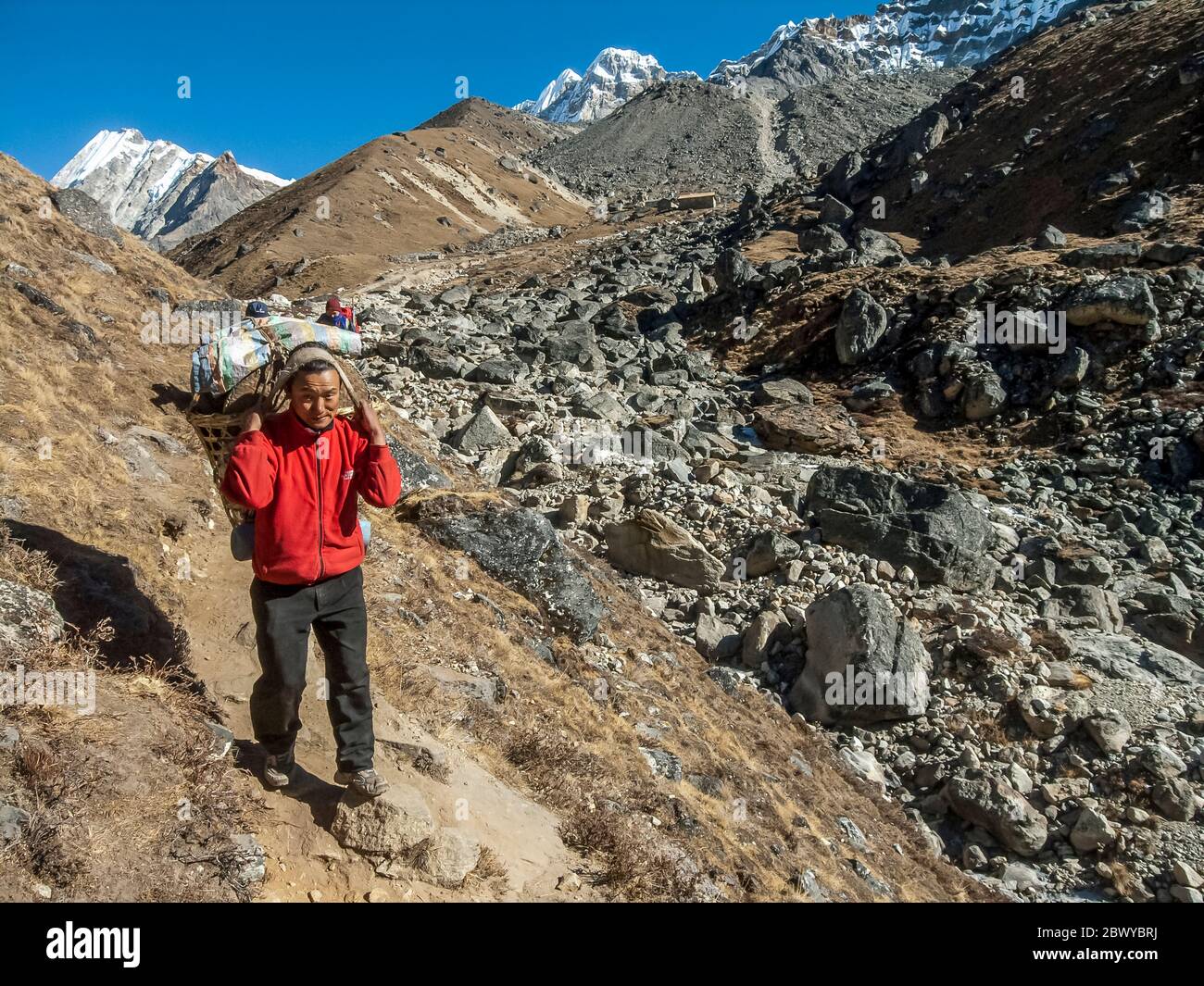 Nepal. Trekking a Mera Peak. Sentiero trekking sotto l'insediamento di Khare con un portatore carico pesante in rotta per Dignag Foto Stock