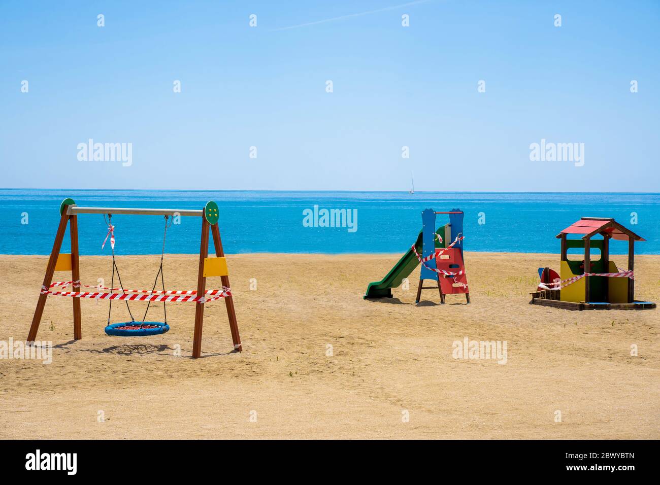 Parco giochi chiuso su una spiaggia a causa della pandemia COVID-19. Ruotare e far scorrere con nastro di protezione. Foto Stock