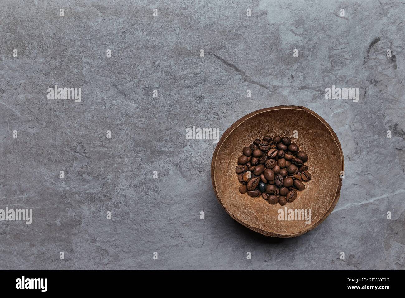 Vista dall'alto dei chicchi di caffè tostati in conchiglia di cocco su rustico sfondo di legno, fotografia di vita con chicchi di caffè tostati Foto Stock