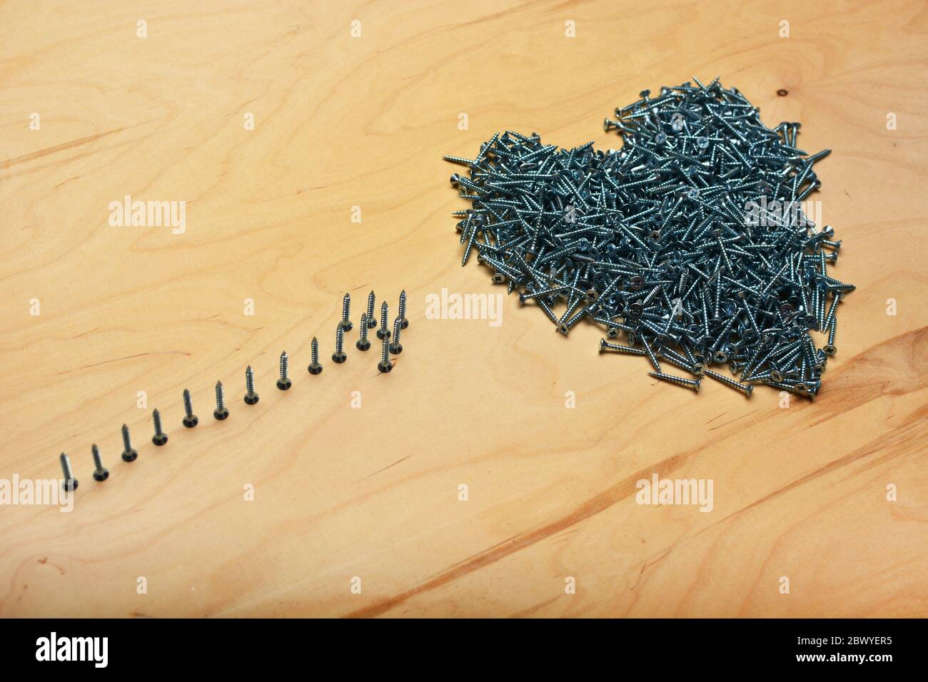 Simboli a cuore e freccia realizzati con viti metalliche su una lamiera di legno compensato. Attrezzature per la produzione di mobili e strumenti per la riparazione di appartamenti. Foto Stock
