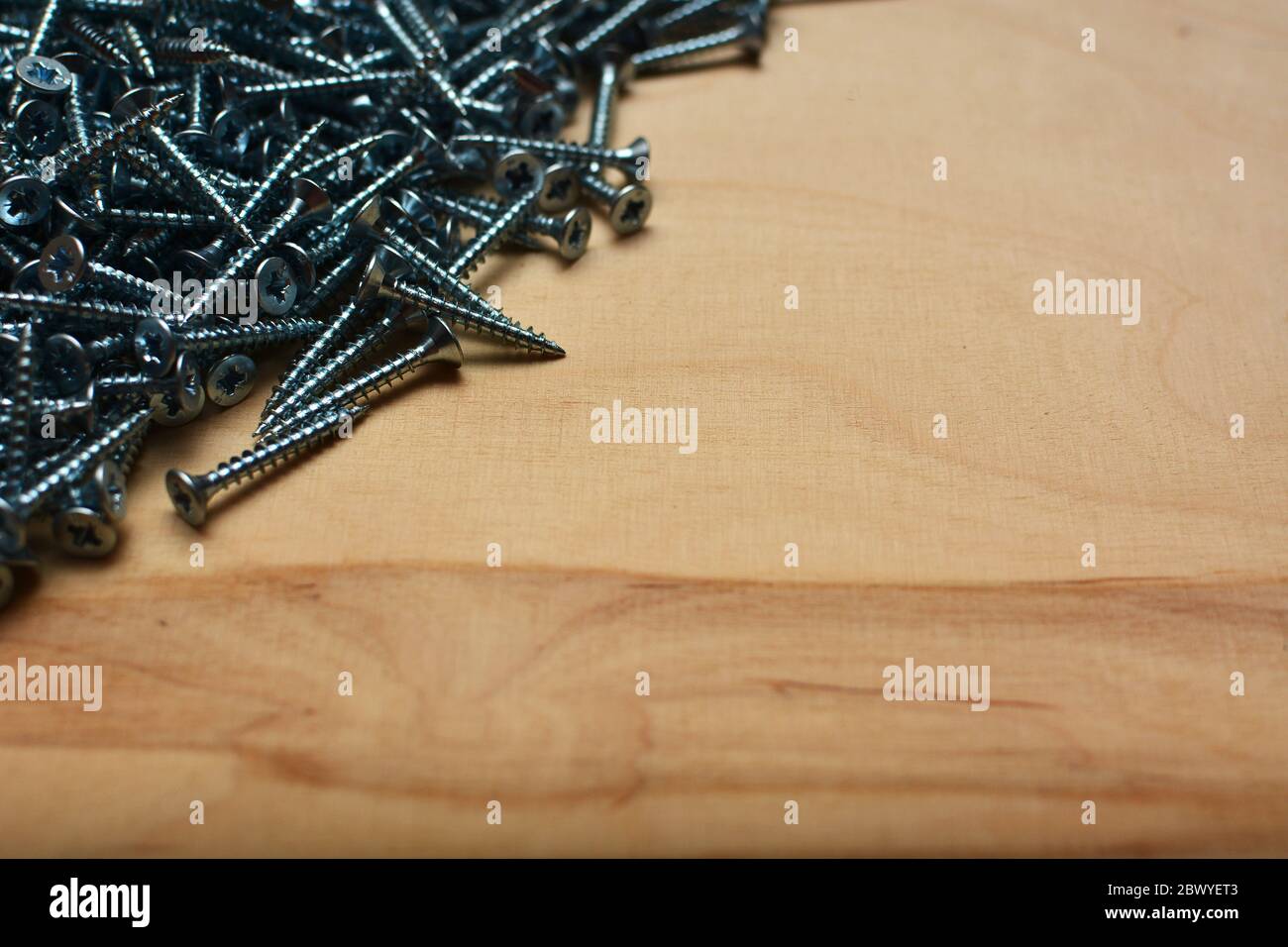 Viti metalliche su un foglio di legno compensato. Attrezzature per la produzione di mobili, attrezzature per la riparazione di hardware e appartamenti. Sfondo per impiallacciatura industriale. Foto Stock