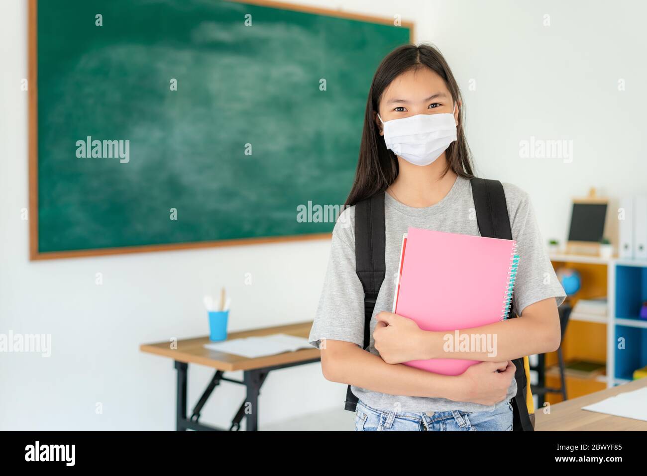 Gli studenti primari asiatici ragazza con zaino e libri che indossano maschere per prevenire lo scoppio di Covid 19 in classe mentre torna a scuola riaprono i loro s. Foto Stock