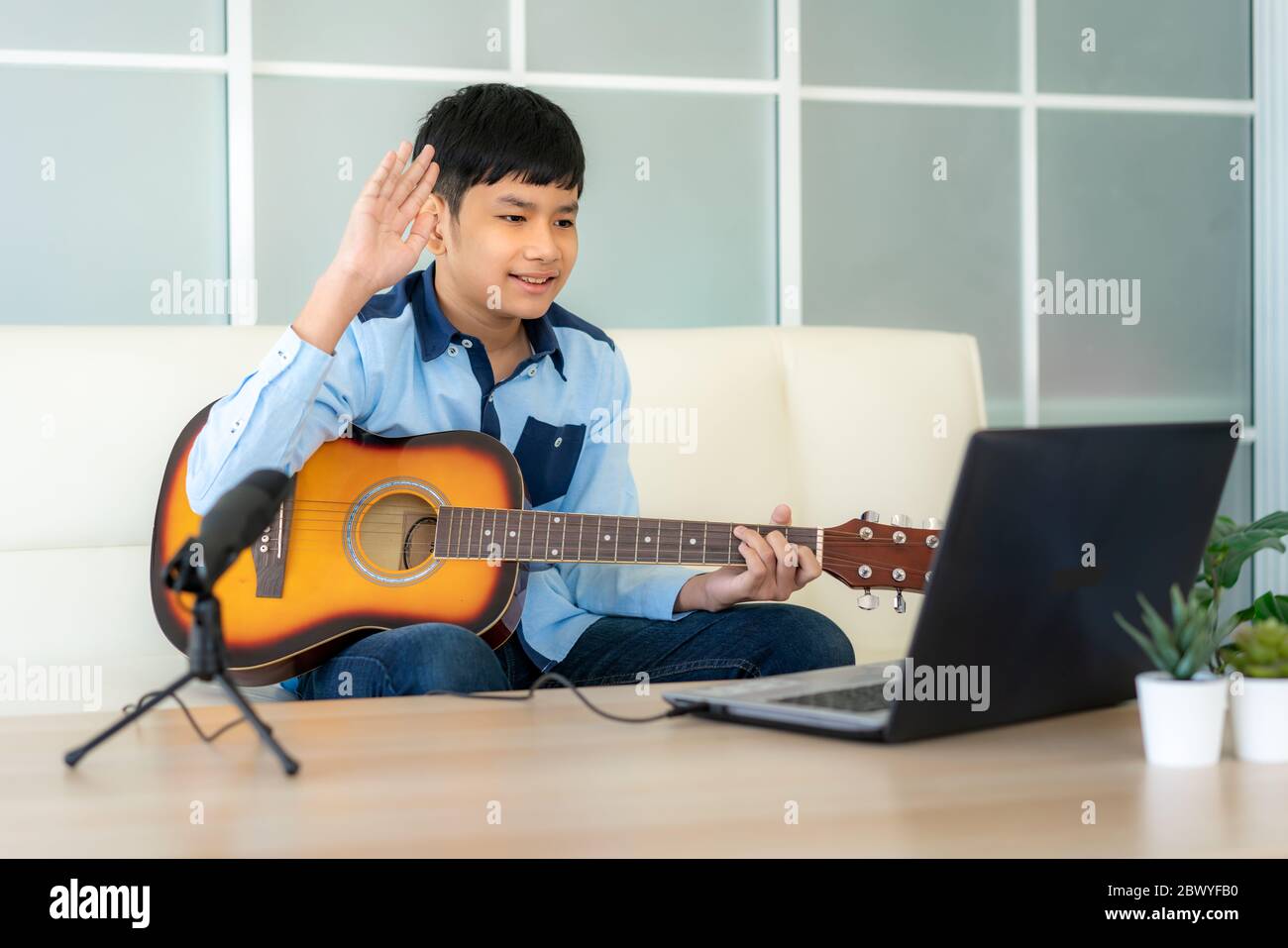 Ragazzo asiatico che suona chitarra acustica virtuale happy hour meeting per giocare musica online insieme ad un amico in videoconferenza con un laptop per un m online Foto Stock