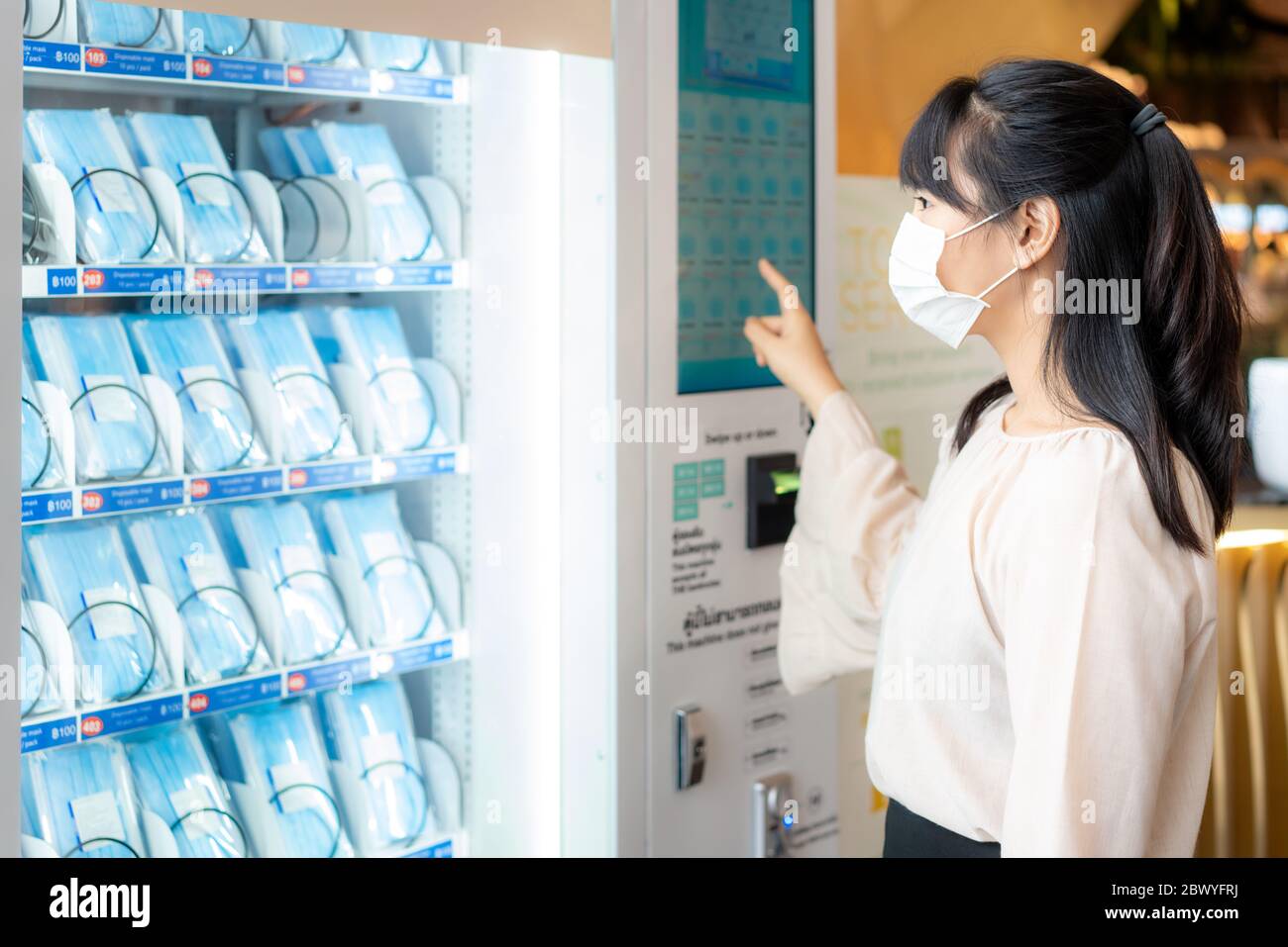 Donna asiatica che indossa maschera utilizzando il distributore automatico maschera per acquistare maschera per la diffusione protettiva di malattia coronavirus Covid-19 nel centro commerciale di Bangkok, Foto Stock